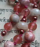 Close up view of transparent pink Cherry Quartz beads; 8mm Rhodochrosite beads with bands of cream, dark pink, and brown; faceted White Agate rondelles framed with 4mm rose Czech glass beads. The knots between the beads and bead units protect and showcase the beads in this design.