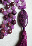 Close up view of 15x30mm oval Purple Crazy Lace Agate guru with vibrant swirling patterns and whorls. A bright purple tassel spills from the base of this focal bead.