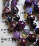 Close up view of deep purple Impression stone beads with faceted Black Agate, dark purple matte Amethyst and gray Mystic Aura beads. Variegated purple knots between beads protect and showcase the beads beautifully in this one-of-a-kind mala design.