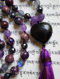 Close up view of heart-shaped Obsidian guru with a variegated purple tassel spilling from the base of this focal bead.