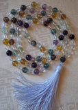 8mm Rainbow Fluorite beads in blue, purple, yellow, green, and burgundy. 6mm faceted Quartz Crystal and matte Mystic Aura beads. A Blue Fluorite guru bead brings this design full circle with a powder blue sutra/tassel.