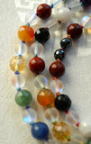 Close up view of 8mm red Apple Jasper, Orange Agate, yellow faceted Citrine, green African Jade, faceted Blue Agate, faceted Black Onyx; 6mm Mystic Aura Crystal beads and faceted Black Agate beads. Variegated knots between the beads protect and showcase the beads of this design beautifully.