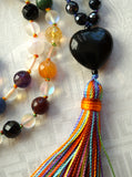 Close up view of 5x25mm, heart-shaped black Obsidian guru with a variegated, rainbow tassel spilling from the base of this focal bead.