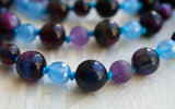 Close up view of deep purple and blue Rainbow Tiger Eye beads, light blue faceted Aqua Jade, and purple matte Amethyst beads. The parrot-blue knots between the beads showcase and protect the beads in this one-of-a-kind design.