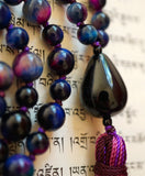Close-up view of teardrop-shaped black Onyx guru, which pairs beautifully with the Rainbow Tiger Eye beads and the variegated purple tassel that spills from the base of the guru bead.