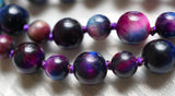 Close up View of bright blue, pink, purple Rainbow Tiger Eye beads. Variegated purple knots protect and showcase the beads of this one-of-a-kind design.