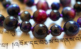 Close up view of 8mm and 6mm Rainbow Tiger Eye beads. The colors range from deep purple, fuchsia, and cobalt blue. Variegated purple knots between the beads protect and showcase the beads of this one-of-a-kind design.