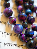 Close-up view of deep purple, blue, and pink Rainbow Tiger Eye beads. The knots between the beads protect and showcase the beads of this one-of-a-kind mala design.