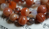 Close up view of 8mm/6mm red orange Botswana Agate beads with white bands; 6mm faceted Madagascar Dendritic Agate beads in smoky gray and white. Cinnamon brown knots between beads protect and showcase the beads in this design.
