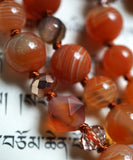 Close up view of red orange Botswana Agate beads with white bands. 8mm star cut Madagascar Dendritic Agate bead framed with rose gold crystals. Cinnamon brown knots between each bead protect and showcase the beads of this design.