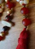 Close up view of double matte Carnelian guru with gold spacer between beads. This bead unit functions as the guru bead of this design. A bright red tassel spills from the base of this bead unit.