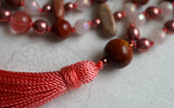 Close up view of 14mm  round Red Porcelain Jasper guru with salmon pink tassel spilling from the base of the bead.