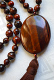 Close up view of 15x30mm Red Tiger Eye guru with chocolate brown tassel spilling from the base of the bead.