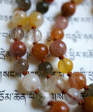 Close up view of Rutilated Quartz beads in yellow, red, orange, gray, and white hues. The cinnamon brown knots between each bead protect and showcase the beautiful beads of this design.