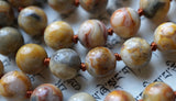 Close up view of 8mm Sage Agate beads with white, creamy yellow, light brown, and gray swirls, whorls, and hues. Each bead is separated with a cinnamon brown knot. The knots help to protect and showcase the beads in this mala.
