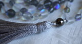 Close up view of simple gray metal guru.  A dove gray tassel spills from the base of this bead.