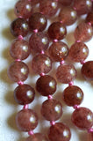 Close up view of 8mm Strawberry Quartz beads. Purplish red with tiny flecks that resemble strawberry seeds. Dusty rose knots between the beads protect and showcase the beads of this design.
