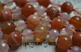 Close up view of 8mm banded Red Botswana Agate beads, ranging in color from red, orange, and peach. 6mm faceted White Agate. Soft salmon colored knots showcase and protect the beads in this design.