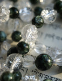 Close up view of 8mm clear Crackle Quartz Crystal beads; dark forest green Seraphinite beads with feather-like white and silver  inclusions; 6mm starcut Quartz Crystal beads ; white knots between beads protect and showcase each bead. 