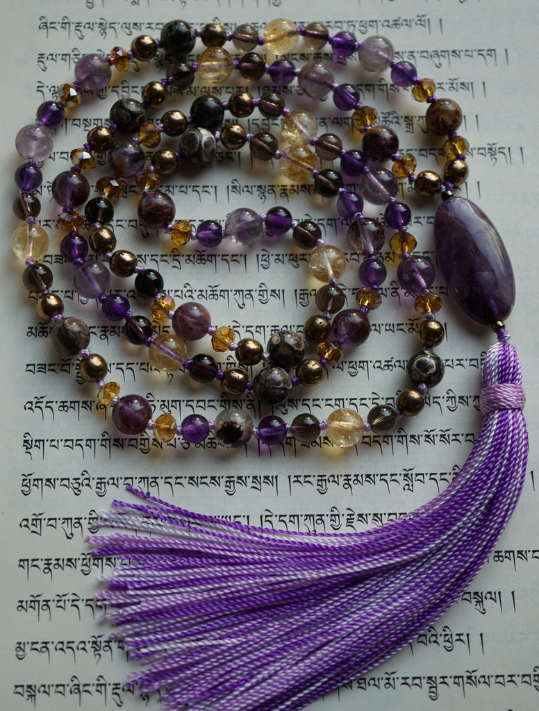 Full view of mala with 8mm purple Cacoxenite, bright translucent yellow Citrine, dark brown Turritella Agate beads. 6mm dark purple Amethyst, translucent brown Smoky Quartz, bronze Czech glass, and amber rondelle crystals. 15x30mm dark purple Amethyst guru (oval) and variegated purple sutra (cord) and tassel.