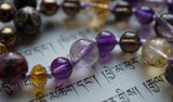 Close up view of 8mm pale purple Cacoxenite, dark purple Amethyst, bright yellow Citrine, and dark amber rondelle crystal beads. This mala is hand-knotted.  The knots protect and showcase the beads in the design.
