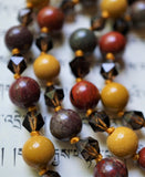 Close up view of 8mm Apple Jasper beads in bold red, brown, and gray. 8mm Golden Mookaite, and 6mm faceted translucent brown Smoky Quartz beads with goldenrod knots between each bead.