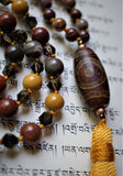close up view of barrel-shaped Dzi Agate guru. Rustic red, brown, and gray  colors complement the beads of this hand-knotted mala.