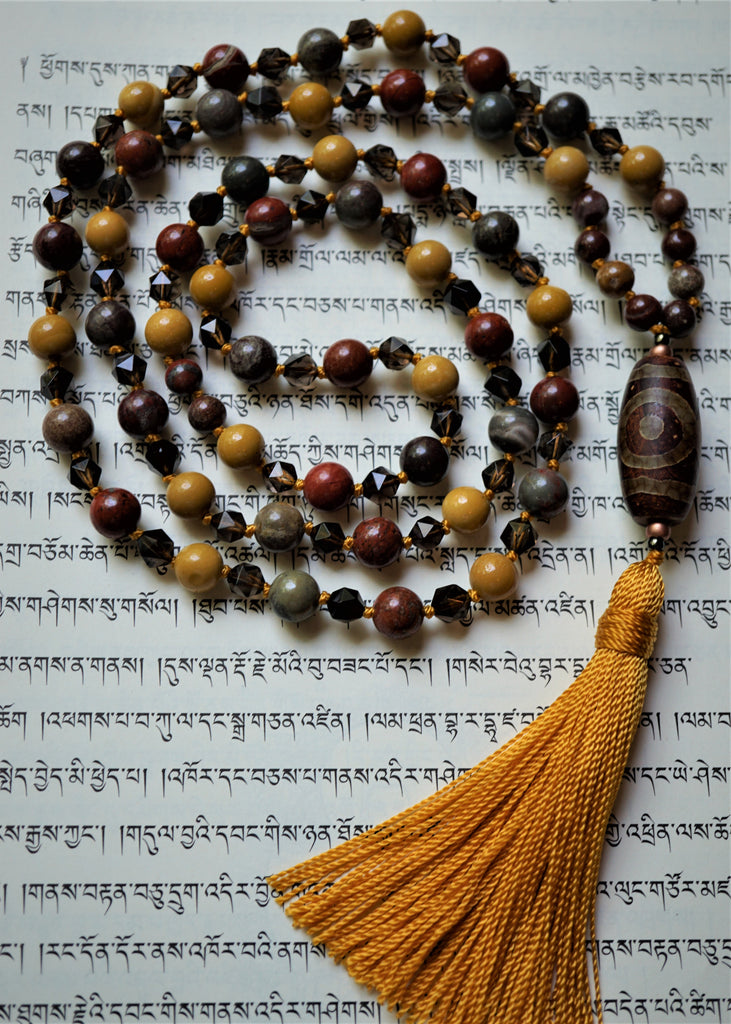 full view of Fall Equinox mala. 8mm Red Apple Jasper, Golden Mookaite; 6mm Apple Jasper and faceted Smoky Quartz beads with barrel-shaped red and brown Dzi Agate guru and goldenrod sutra and tassel. This one-of-a-kind, hand-knotted mala is perfect for the upcoming fall season.