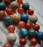 Close up view of bright orange Fire Agate, Bold Blue Apatite, Turquoise Cuprite, and earthy tones of Fossil jasper beads. A bright orange sutra with knots in between each bead showcases and protects the beads.