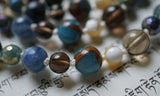 close up view of sky blue Mosaic Quartz (blue with brown inclusions), Smoky Quartz (translucent brown), Mother of Pearl (cream and white), blue Kyanite, and faceted  rainbow plated Jasper beads.